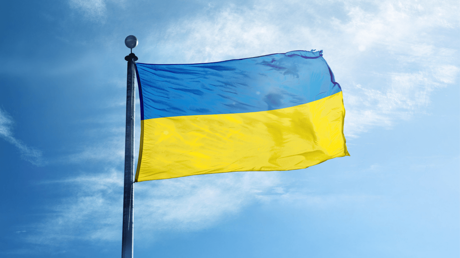 A photo of the Ukrainian flag flies in front of of a bright blue sky.