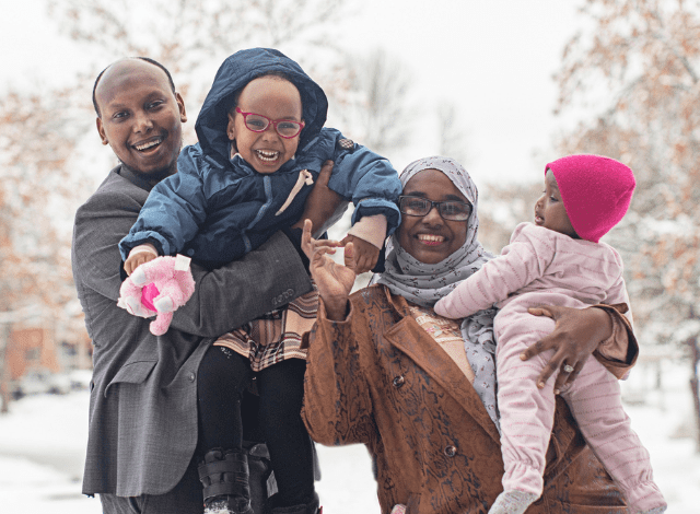 A somali family smile as they stand in the snow wearing coats.