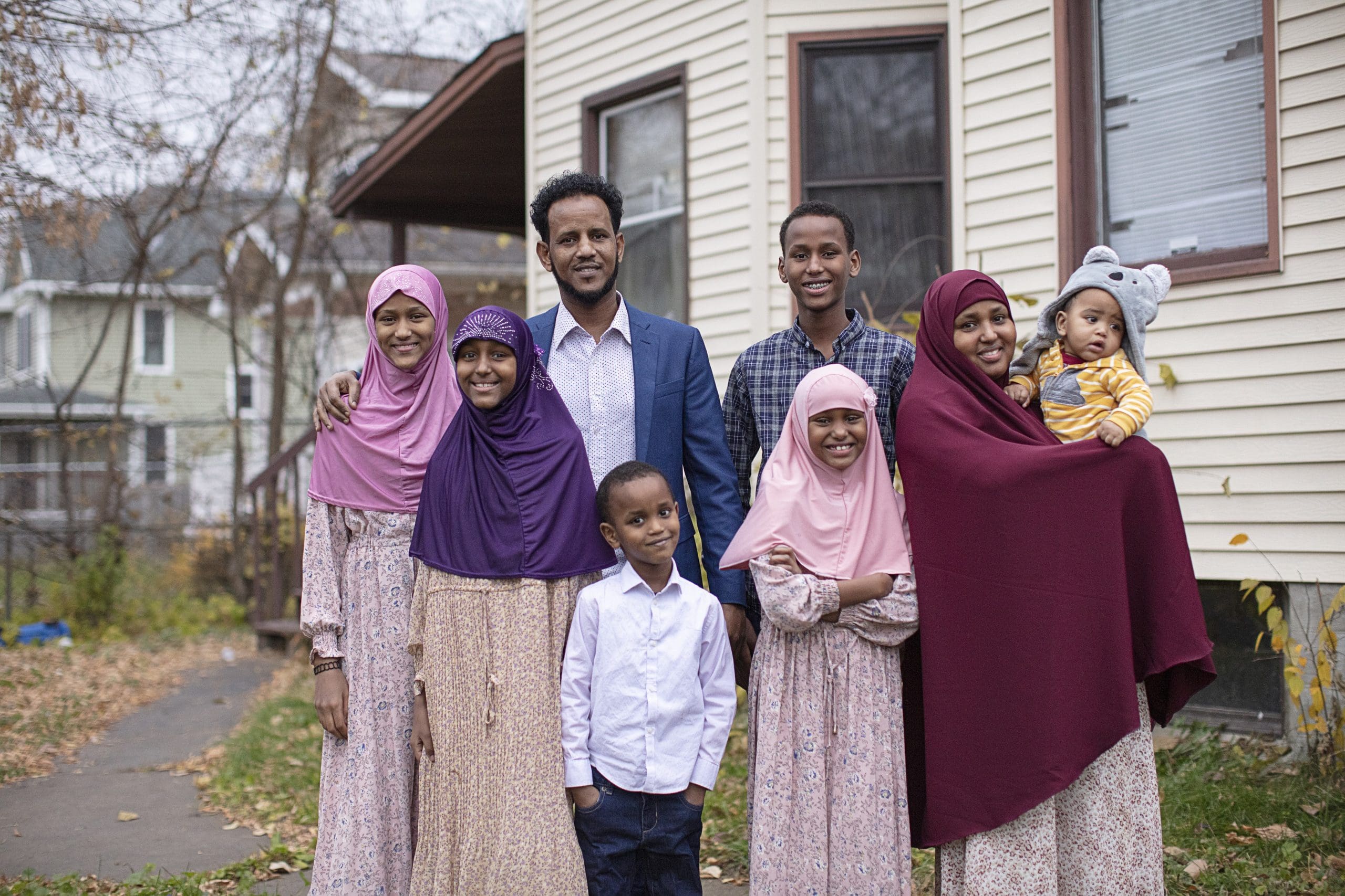 A reunited family of New Americans poses outside their home.