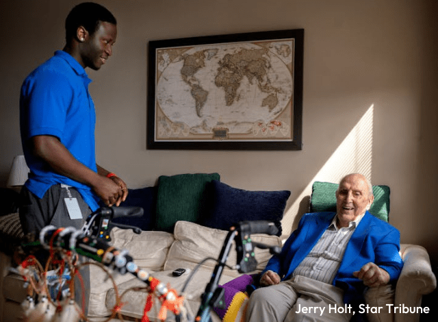 A black young man in a blue shirt talks to a white old man in a blue sweater