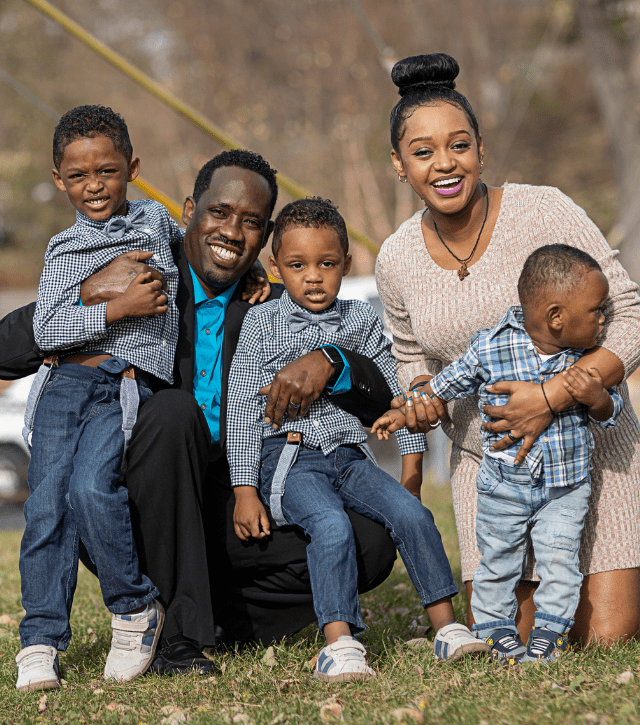 A mother and father hugs their three young sons.