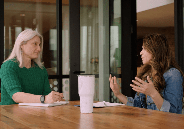 Two women talk in a conference room.